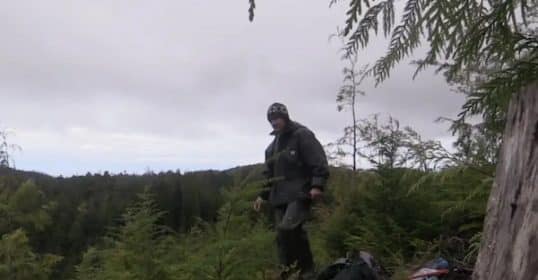 A person standing in a forest clearing with camping gear, dispelling survival myths in Podcast #869.