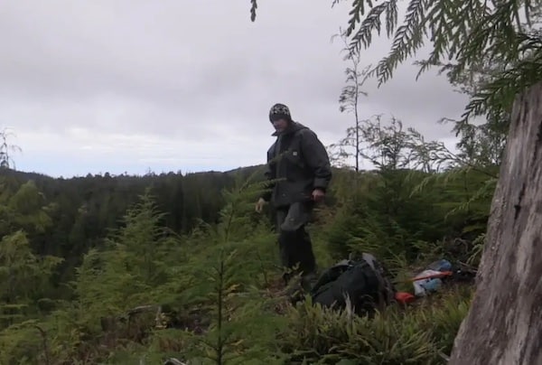 A person standing in a forest clearing with camping gear, dispelling survival myths in Podcast #869.