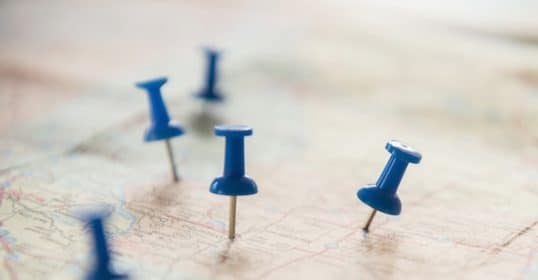 Blue pushpins decide locations on a map for where to live.
