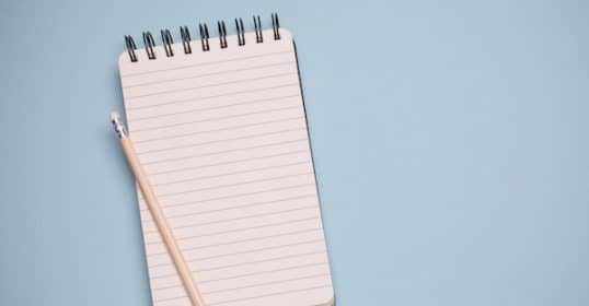 A blank lined notebook for productivity lists with a pencil on a blue background.