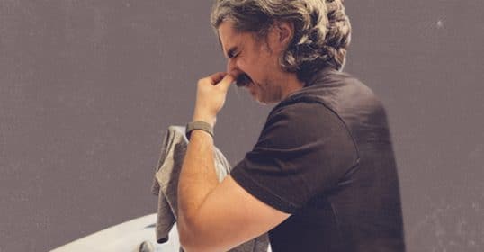 Man pinching the bridge of his nose in frustration or fatigue, overwhelmed by how to get the stink out of synthetic workout shirts.