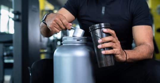 Man preparing a protein shake at the gym, using fitness supplements that actually work.