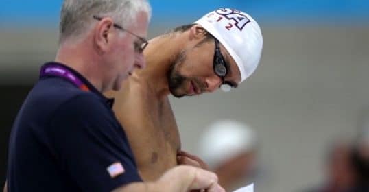 Swimmer reviewing performance times and discussing golden rules with coach at the poolside.