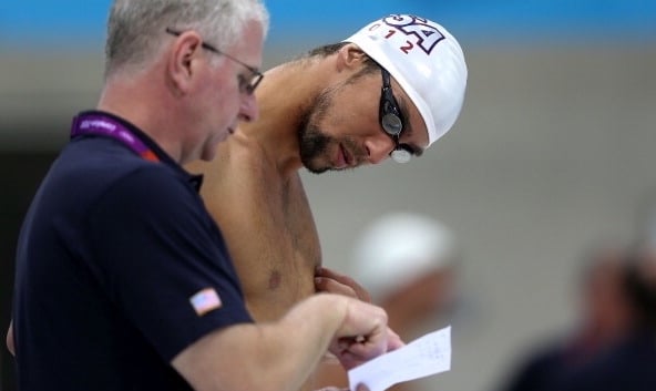 Swimmer reviewing performance times and discussing golden rules with coach at the poolside.