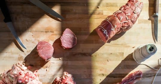 Butcher's table at home with raw meat, knives, and kitchen twine during preparation.