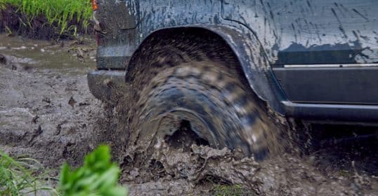 A vehicle's wheel spinning and splashing mud while off-roading, getting unstuck.