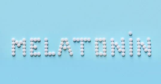 White pills spelling out 'does melatonin work?' on a blue background.
