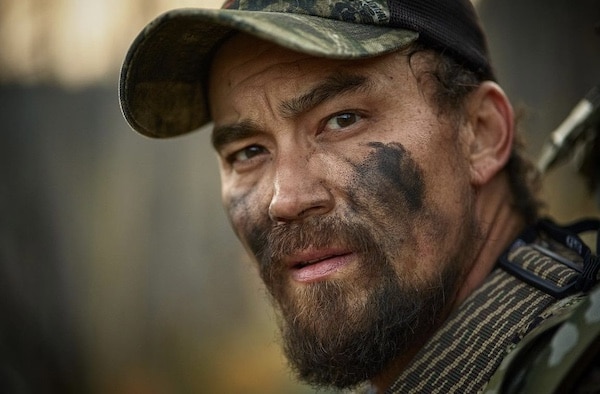A close-up of a man with camouflage paint on his face, wearing military apparel, and looking off-camera during Podcast #902 on "How to Survive the Worst Case Scenario.