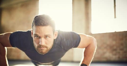 Man doing a morning workout push-up in a sunlit room while listening to Podcast #905.