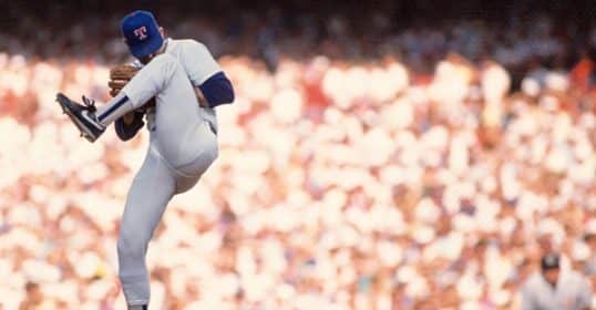 Baseball pitcher Nolan Ryan in mid-throw during a game with spectators in the background.