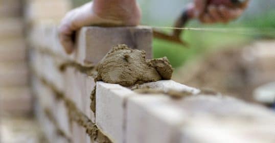 Bricklayer motivated by personal growth, applying mortar to lay bricks.