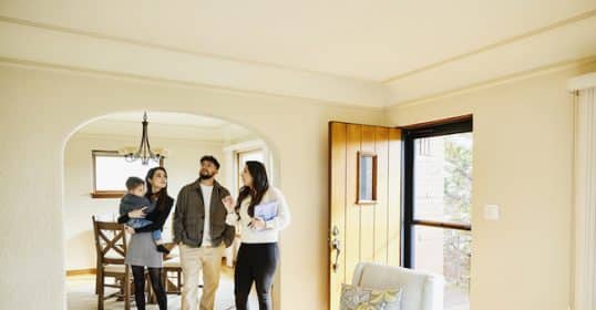 A group of people touring a well-lit, furnished home, with one person appearing to explain features of the house during a home inspection.