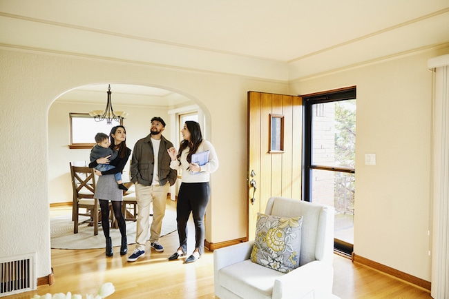 A group of people touring a well-lit, furnished home, with one person appearing to explain features of the house during a home inspection.