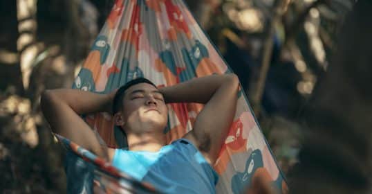 Young man with an unfocused mind relaxing in a colorful hammock outdoors.