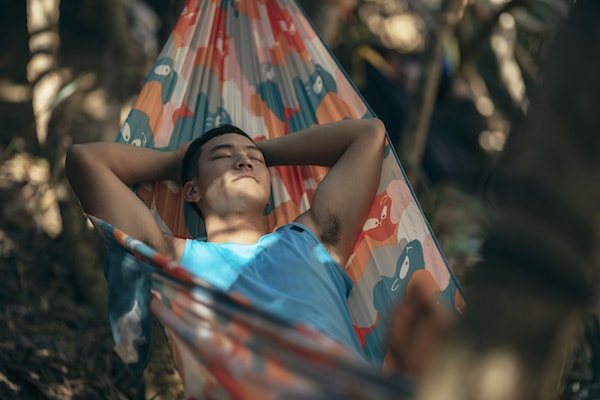 Young man with an unfocused mind relaxing in a colorful hammock outdoors.