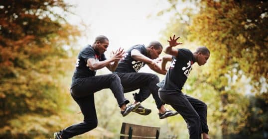 Three individuals demonstrating a synchronized jump over a park bench for a better workout.