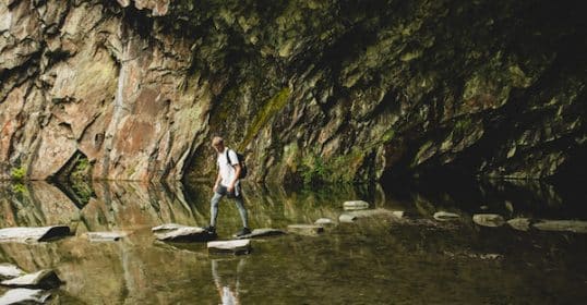 Person stepping on rocks across a shallow water body inside a rocky gorge, contemplating the
