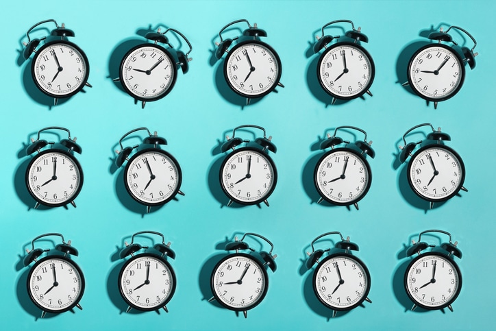 An array of identical black alarm clocks against a teal background, each showing a different time, symbolizes the real reason behind procrastination discussed in Podcast #931.