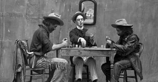 Three men in vintage western attire playing a board game at a table, embodying the history of