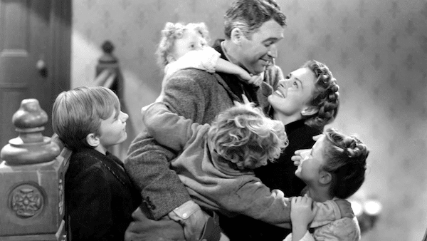 A black and white photo of a happy family moment with two adults and three children embracing each other affectionately after watching classic Christmas movies.