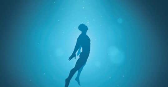 Silhouette of a person swimming underwater with light rays shining through the water, exploring the Science of Immersion.