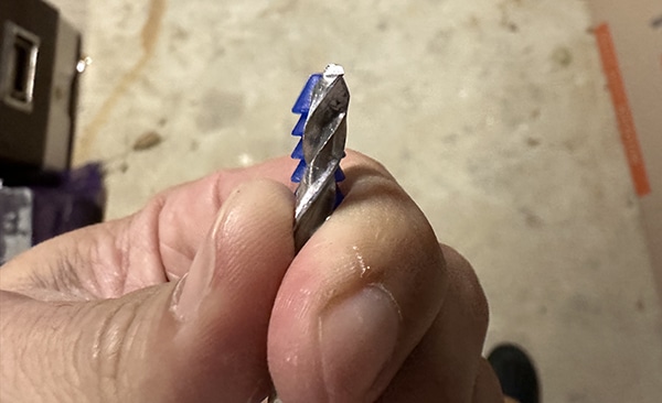 A person holding a drill bit for drywall anchors in their hand.