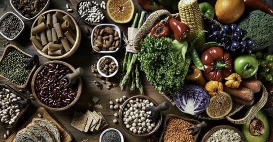 Assorted healthy foods, including fruits, vegetables, grains, and nuts rich in fiber, displayed on a wooden table.