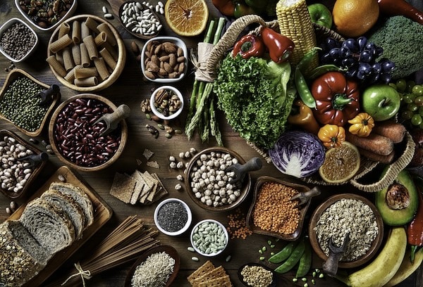 Assorted healthy foods, including fruits, vegetables, grains, and nuts rich in fiber, displayed on a wooden table.