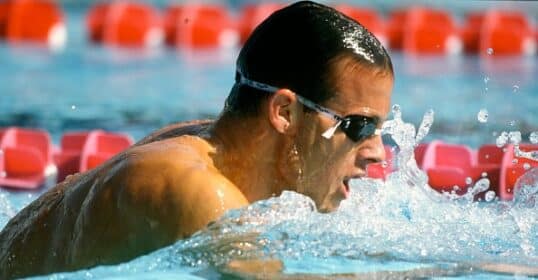 A man swimming in a pool with goggles on, exemplifying the mundanity of excellence.