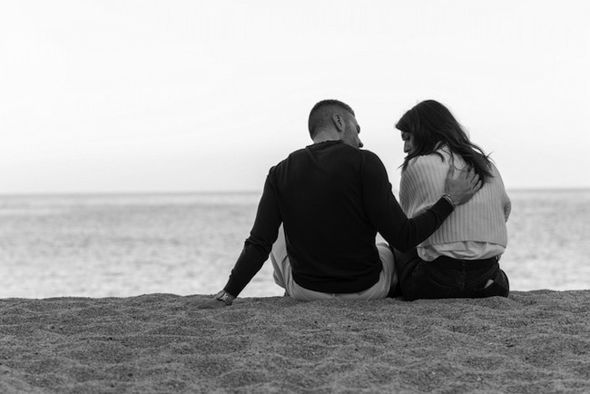A black and white photo of a couple sitting on the beach.