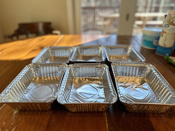 Five aluminum foil pans containing a super easy and high-protein breakfast bake, neatly arranged on a wooden table.