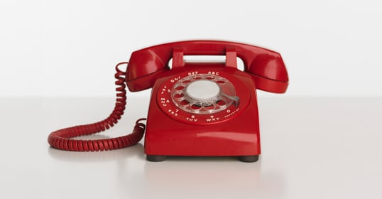 A red rotary dial telephone, typically used by a hostage negotiator for handling difficult conversations, with its receiver on the left, set against a plain white background.