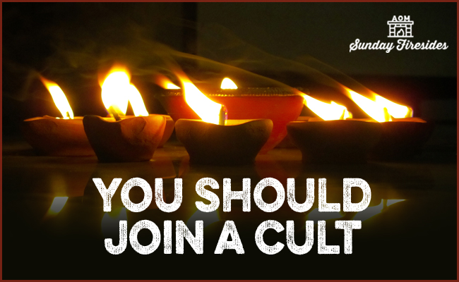 Caption: "Several lit oil lamps on a surface with the bold statement 'You Should Join a Cult' overlaid, accompanied by 'Sunday Firesides' logo.