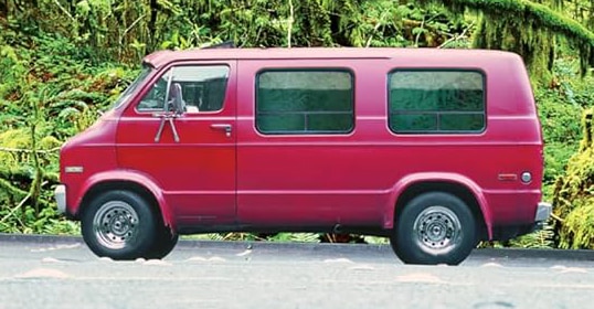A red van parked on a road surrounded by lush greenery, embodying the spirit of an American adventure.