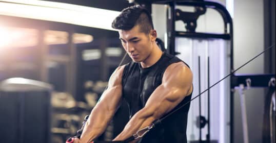 A person in a gym using a cable machine for strength training, performing a chest exercise with focused expression, showcasing the efficacy of cable machine workouts.