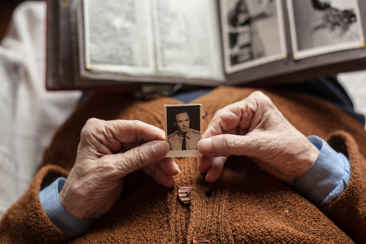 Elderly person holding a small, old photograph in front of an open photo album, recovering nostalgic memories.