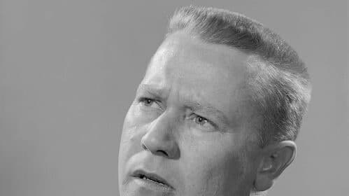 A black and white portrait of a man in a suit and tie with a contemplative expression, looking slightly upwards, radiates an aura of metacognition.