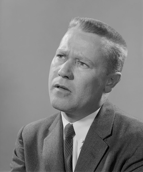 Black and white portrait of a man with short hair, wearing a suit, dress shirt, and tie, looking slightly upward with a thoughtful expression that suggests deep self-awareness.