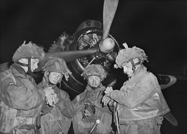 Cuatro soldados con uniforme militar y cascos consultan sus relojes delante de la hélice de un avión, posiblemente coordinando una operación.  Esta asombrosa escena está capturada en una de las fotografías raramente vistas del Día D.
