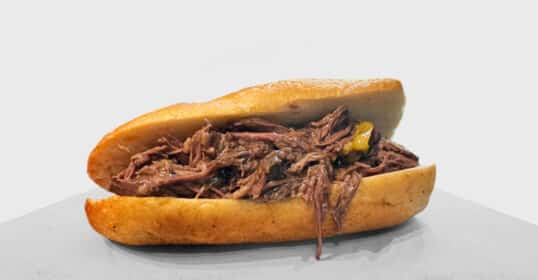 A 4-Ingredient Italian Shredded Beef sandwich with peppers in a toasted bun on a plain background, perfect for Lunchtime Meal Prep.