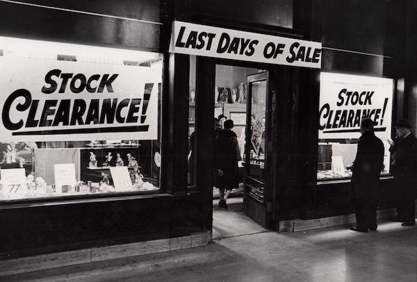 A store with large signs in the windows reading "50% Off!" and "Last Days of Sale at AoM Store." Shoppers can be seen looking through the windows.