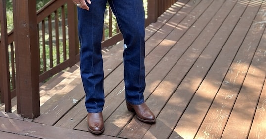 A person in blue jeans and brown shoes stands on the wooden deck, looking every bit the modern-day pardner surveying the horizon.