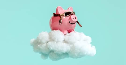 A piggy bank with aviator goggles sits on a fluffy cloud against a turquoise background, like an auto draft of whimsical imagination.