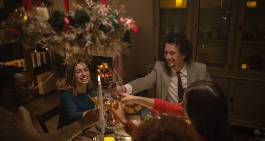 Four people are gathering around a beautifully set table, clinking glasses and enjoying the art of hosting in a festive, warmly lit setting.