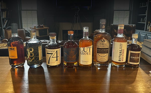 Eight bottles of alcohol-free spirits, including the best zero-proof whiskey, are lined up on a wooden table, with various labels and designs visible.