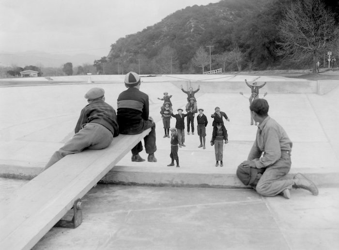 Children play on a seesaw in an outdoor park, their joyful laughter echoing as others stand and cheer. A son eagerly awaits his turn, hoping to join the fun.