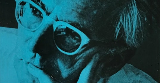 A close-up of an older person wearing glasses, resting their chin on their hand with a contemplative expression, reminiscent of Viktor Frankl. The image has a blue tint that echoes the depth found in