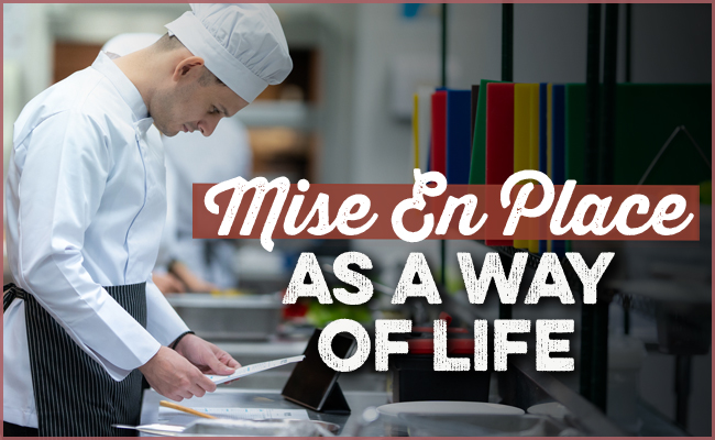 A chef in a white uniform studies a document in the kitchen, embodying the motto "Mise En Place: The Chef's Secret to a Productive Life.