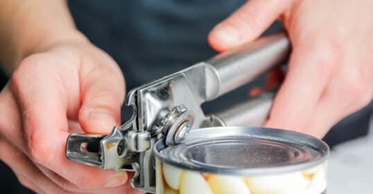 A person uses a manual can opener to access a tin of white beans, perfect for cheap eating and meal prep.