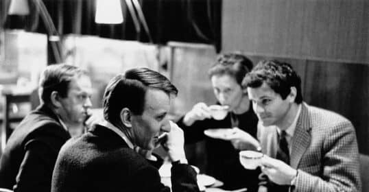 Four people sit at a table in a café, engaged in conversation while drinking from teacups.